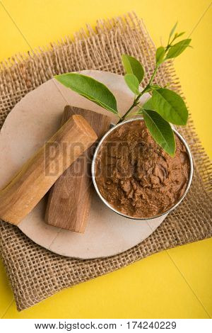 Ayurvedic Chandan powder or sandalwood paste in silver bowl with sticks and leaves placed over sahan or sahana or circular stone base for creating paste