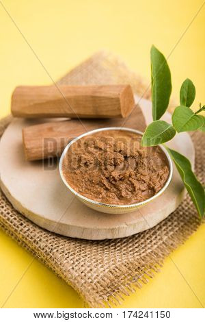 Ayurvedic Chandan powder or sandalwood paste in silver bowl with sticks and leaves placed over sahan or sahana or circular stone base for creating paste