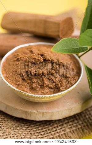 Ayurvedic Chandan powder or sandalwood paste in silver bowl with sticks and leaves placed over sahan or sahana or circular stone base for creating paste