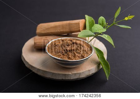 Ayurvedic Chandan powder or sandalwood paste in silver bowl with sticks and leaves placed over sahan or sahana or circular stone base for creating paste