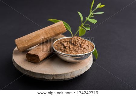 Ayurvedic Chandan powder or sandalwood paste in silver bowl with sticks and leaves placed over sahan or sahana or circular stone base for creating paste