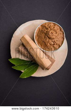 Ayurvedic Chandan powder or sandalwood paste in silver bowl with sticks and leaves placed over sahan or sahana or circular stone base for creating paste