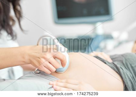 Crop of professional doctor using ultrasound equipment,  screening of pregnant woman. Doctor in white uniform touching stomach by tool of female.