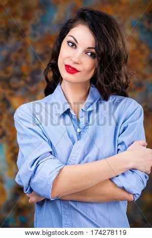 Closeup portrait of young brunette woman in blue shirt, dark studio wall background
