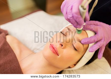 people, beauty, cosmetology, exfoliation and technology concept - beautiful young woman having microdermabrasion facial treatment with crystals in spa