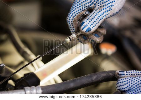 car service, repair, maintenance and people concept - auto mechanic man with dipstick and lamp checking for motor oil level at workshop