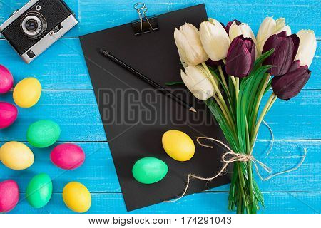 colorful easter eggs and bouquet of tulips on wooden background with space for a text, top view