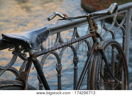 black old bike leaning on the iron bridge above the river