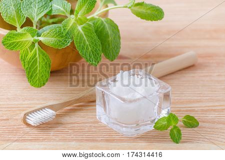 alternative natural toothpaste coconut oil and wood toothbrush closeup mint on wooden background