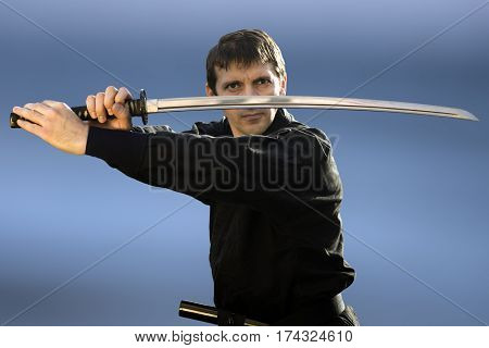 Ninja in black kimono with sword on blue background.