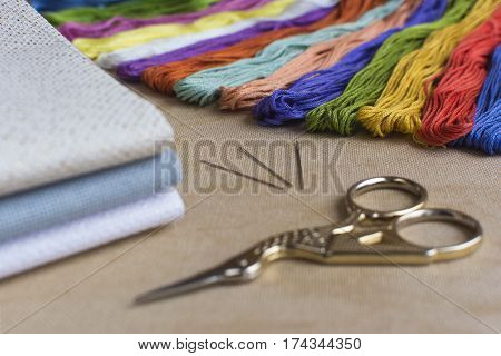 Embroidery and cross-stitch kit on a natural linen background. Focus on the multicoloured threads.