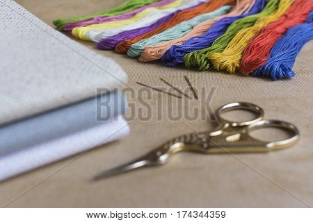 Cross-stitch set for embroidery consisting of canvas needles threads and scissors. Focus on the colourful threads.