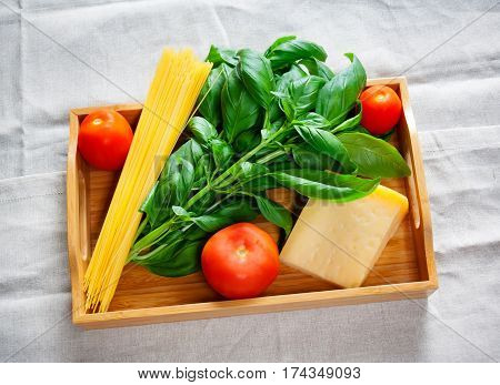 Green basil chunk of parmesan cheese raw cappellini pasta and tomatoes on wooden tray