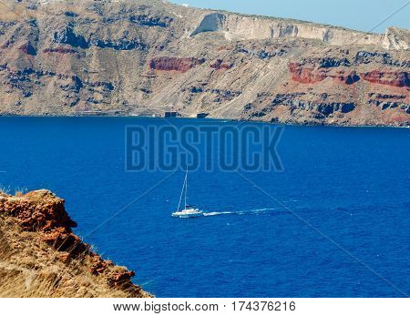 White yacht passes by Cape Bizantin near Santorini island.