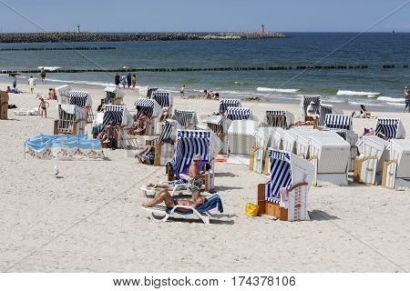 KOLOBRZEG POLAND - JUNE 19 2016: Vacationers enjoy the sunny weather on the sandy beach they are relaxing and sunbathing on the shore of the Baltic Sea many of them use roofed beach chairs