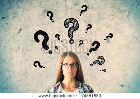 Pretty caucasian girl with question marks on concrete wall background. Questions concept