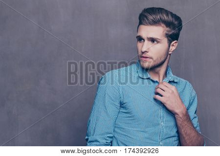 Thoughtful Stylish Man Standing In Front Of Gray Background And Touching His Collar