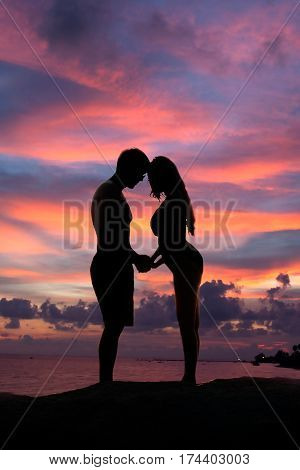 Lovely young adult couple standing on the rocks above tropical sea in Sunset.