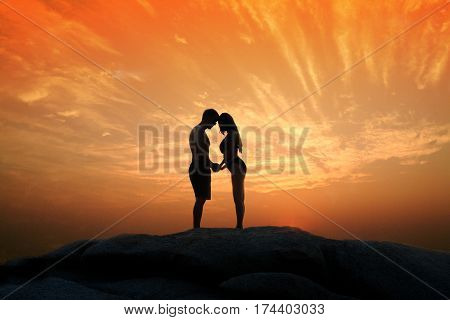 Lovely young adult couple standing on the rocks above tropical sea in Sunset.