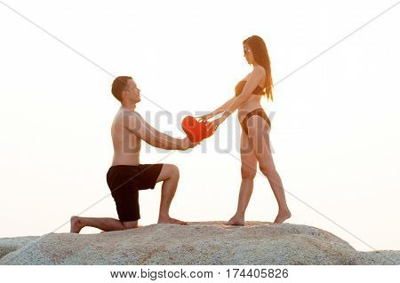 Lovely young adult couple standing on the rocks above tropical sea in isolated.