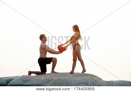 Lovely young adult couple standing on the rocks above tropical sea in isolated.