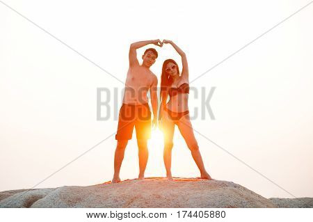 Lovely young adult couple standing on the rocks above tropical sea in isolated.