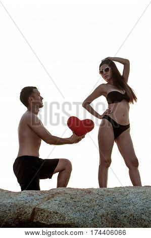 Lovely young adult couple standing on the rocks above tropical sea in isolated.