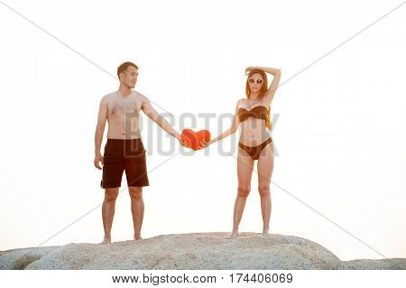 Lovely young adult couple standing on the rocks above tropical sea in Sunset.