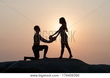 Lovely young adult couple standing on the rocks above tropical sea in Sunset.
