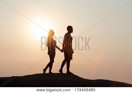 Lovely young adult couple walking on the rocks above tropical sea in Sunset.