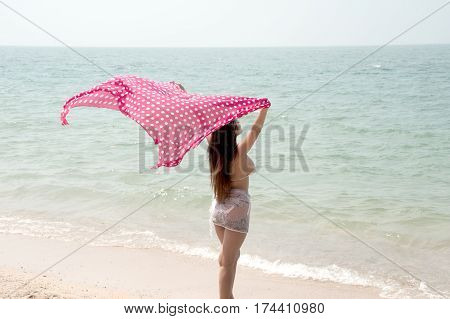 Positive pretty female holding fabric up and expressing gladness on the beach.