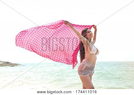 Positive pretty female holding fabric up and expressing gladness on the beach.
