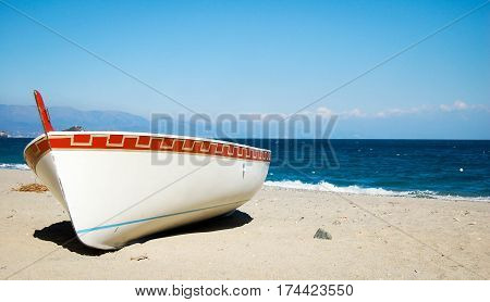 small white boat on a beach with blue sea and sky in the background