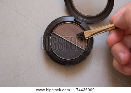 Brown and black shadows for brows brush and female hand on gray background