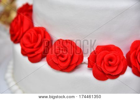 Sweet cakes in the form of red roses decorate the wedding cake with more decorative twigs of white cream. Photographed at a wedding in Novi Sad, Serbia.