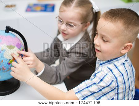 closeup portrait of little schoolchildren are examining globe