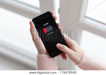 Women hands holding phone with low charged battery screen on background of window