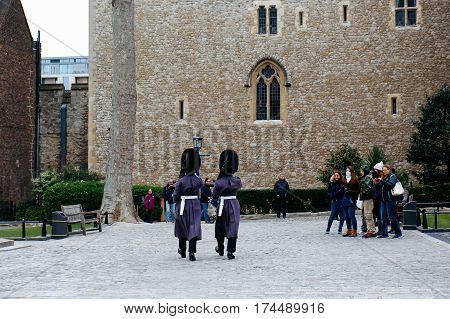 LONDON, UK - MARCH 30, 2016: Tourists watch two Queen's Guards in winter dress marching on the grounds of the Tower of London.