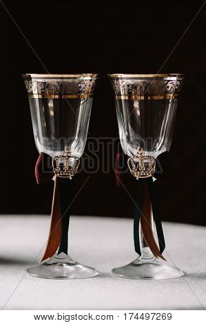 Wedding decorated champagne glasses with the crown, green and red ribbons in the royal style on the gark background