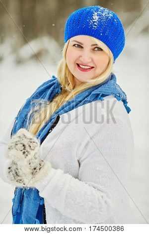 Portrait of smiling plump woman in white and blue dress outdoor in winter park.