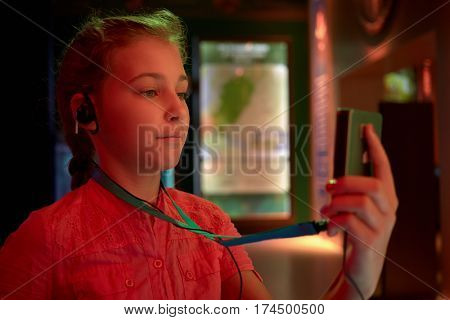 Girl looks at and listens to audioguide at dark museum room.