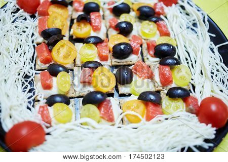 Dark dish with threads of sulguni and many tartines with pieces of olive, red fish and roma tomato.