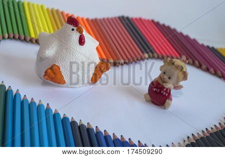 On a white background colored pencils and spread among them figures of white chicken and angel with a red heart on which the inscription "I love you."