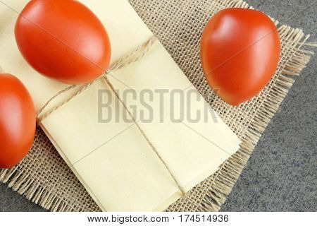 Three fresh red tomatoes and sheets for Italian lasagne on sackcloth and dark background.