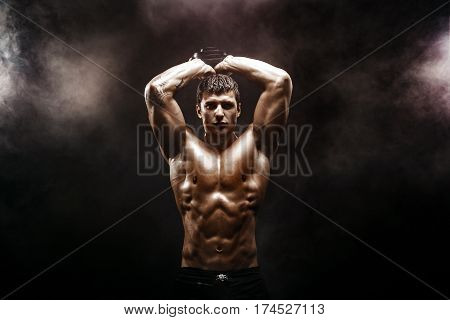 Handsome bodybuilder doing exercise with dumbbell. Studio shot. Smoke.