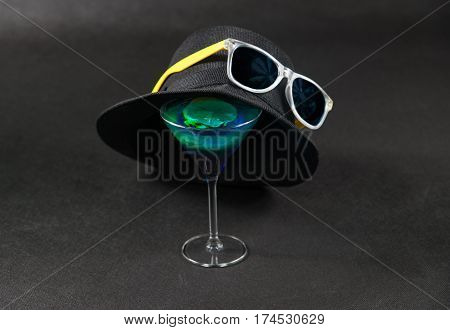 colored drink a combination of blue and green lemon martini glass yellow sunglasses a black hat on the glass party set