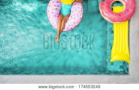 Woman relaxing on donut lilo in the poolside at private villa. Inflatable ring and mattress. Summer holiday idyllic. High view from above.