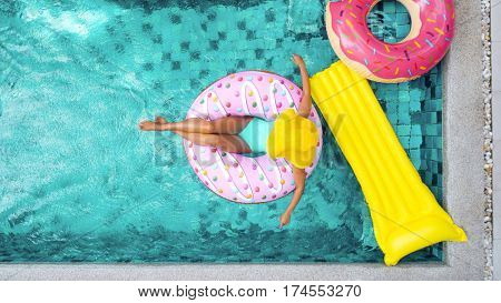 Woman relaxing on donut lilo in the pool at private villa. Inflatable ring and mattress. Summer holiday idyllic. High view from above.