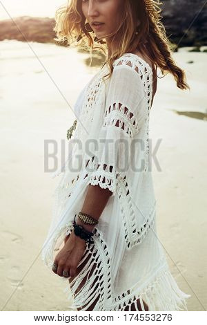 Beautiful boho styled model wearing white crochet swimsuit posing on the beach in sunlight