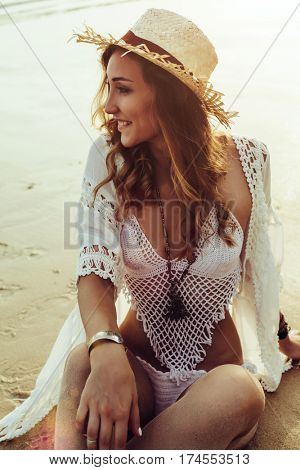 Beautiful boho styled model wearing white crochet swimsuit posing on the beach in sunlight